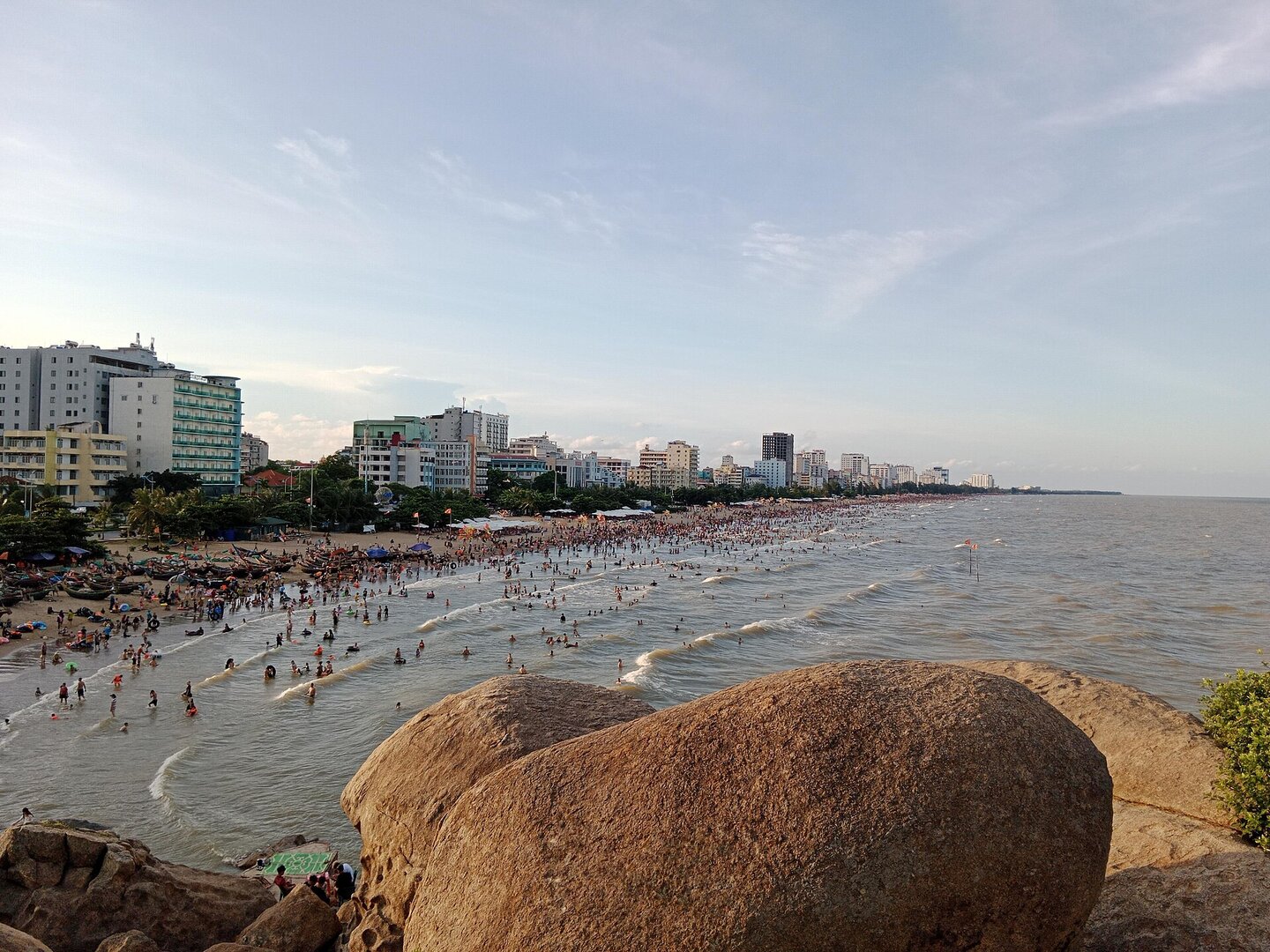 Bãi biển Sầm Sơn nhìn từ hòn Cổ Giải một chiều tháng Bảy, sóng nhẹ, người tắm biển đông kín dọc bờ, dãy khách sạn phía sau.